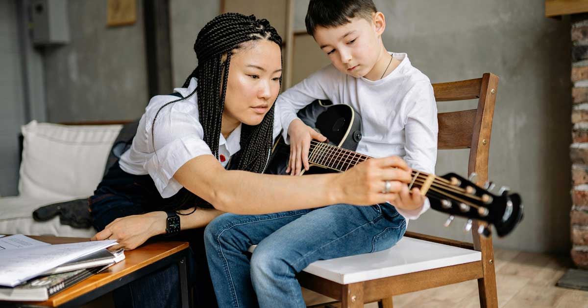 Asian woman teaching guitar to a boy